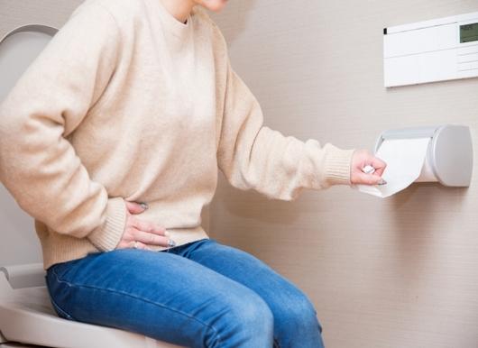 トイレに座ってトイレットペーパーに手を伸ばす女性
