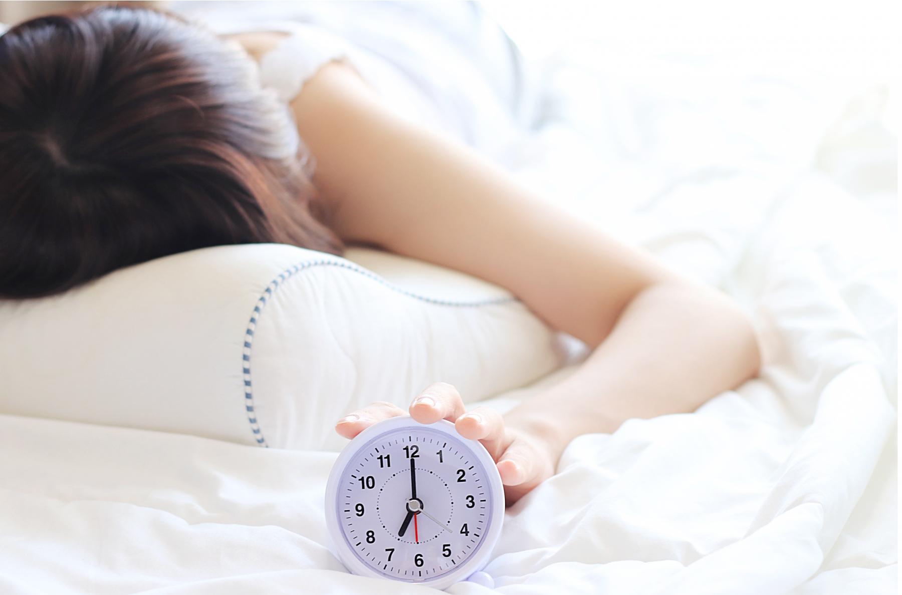 ベッドで目覚まし時計を止める女性