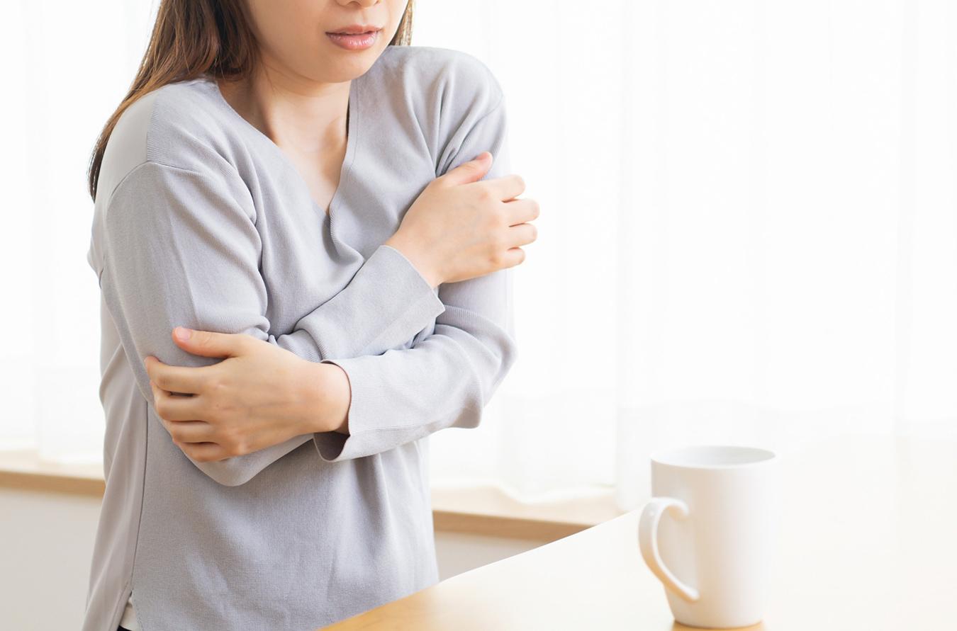 室内で凍える女性とコーヒーカップ