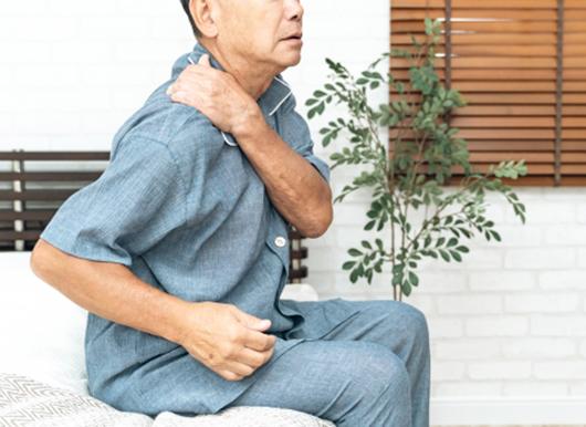 ベッドに腰かけて体の痛みを訴える男性