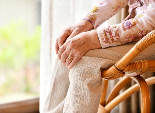 窓際に置いた椅子に腰かける高齢女性