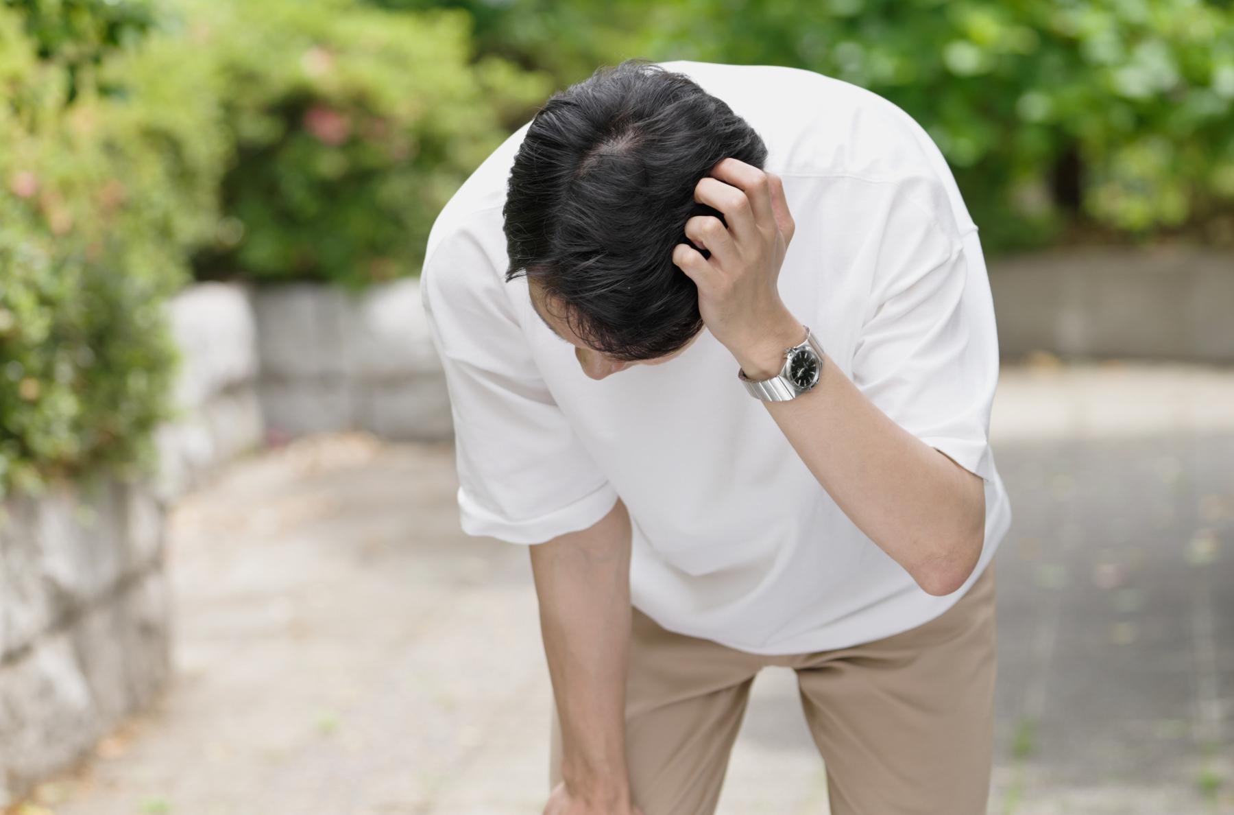 日中に屋外で頭を押さえている男性