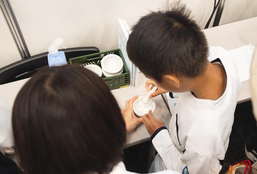 日本調剤の薬剤師のサポートを受けながら、乳鉢と乳棒でラムネを粉砕する男の子