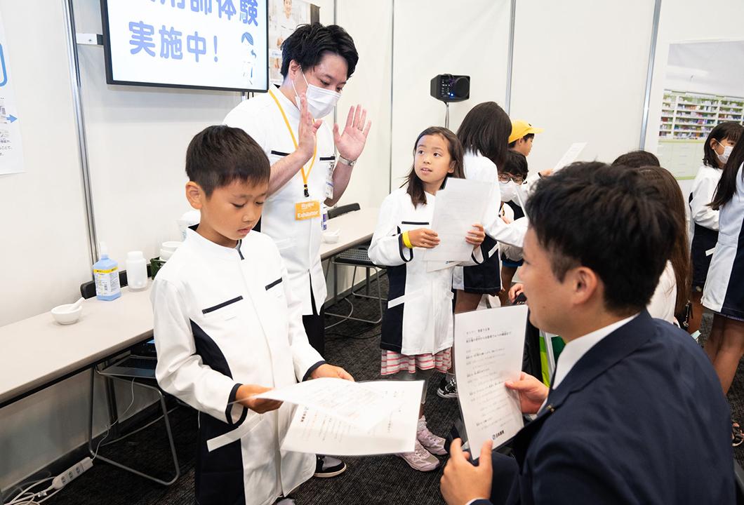 日本調剤の薬剤師のサポートの元、保護者へ服薬指導のロールプレイを行う子どもたち