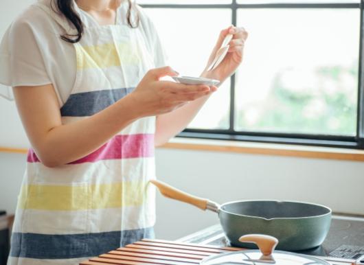 料理を味見皿によそうエプロン姿の女性